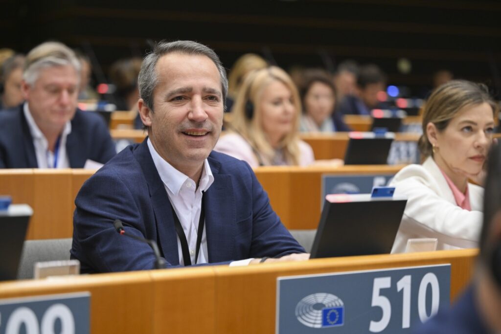 O eurodeputado Sérgio Humberto sorridente sentado no hemiciclo do Parlamento Europeu no lugar 510